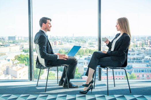 Business people sitting near panoramic window with view on city and talking at break