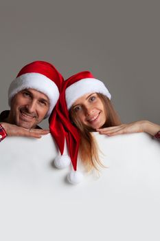 Happy couple in Santa hats holding blank banner with white copy space