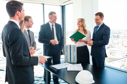 Meeting of architects and business investors, model of modern multi storey residential building house plans and hardhat on table , construction planning concept