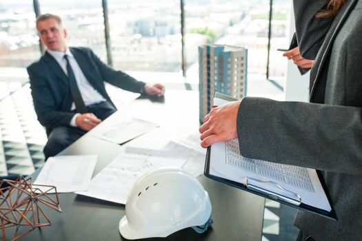 Meeting of architects and business investors, model of modern multi storey residential building house plans and hardhat on table , construction planning concept