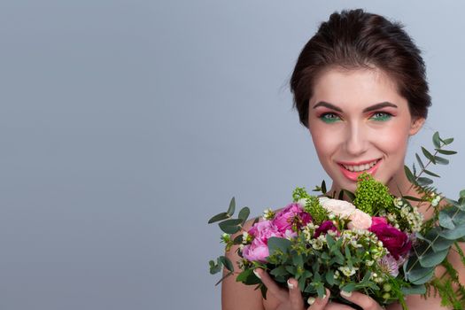 Beautiful woman with stylish make-up holding bouquet of flowers on gray background