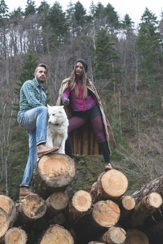 Young woman and men on wood logs in the forest. White dog