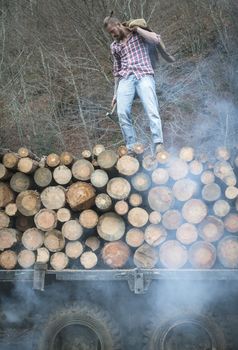 Young man on vintage truck with logs in the forest.