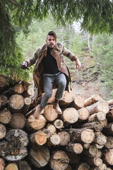 Young men on logs in the forest. Leather and jeans. Pine tree on top