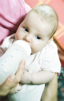 Baby sucks on a bottle. Baby in mother's hands