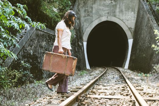 Woman walk on railroad with a suitcase in hands. Vintage style image