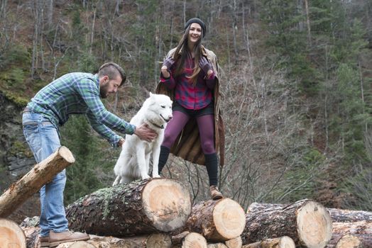 Young woman and men on wood logs in the forest. White dog