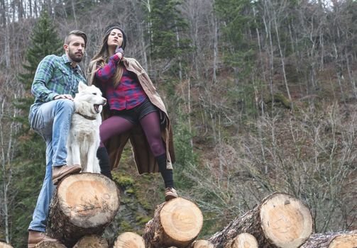 Young woman and men on wood logs in the forest. White dog