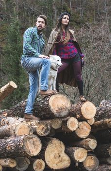 Young woman and men on wood logs in the forest. White dog