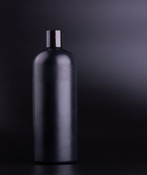 Big black hair shampoo bottle on black background