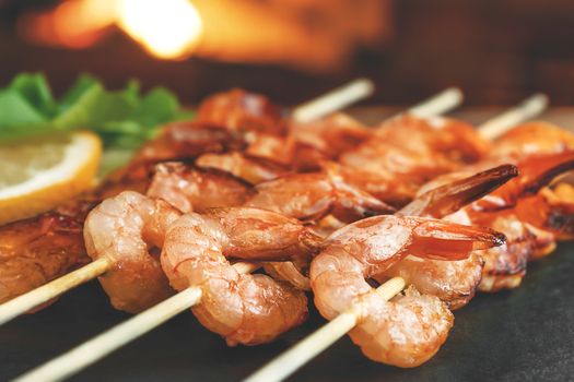 Shrimp fried on skewers with arugula and lemon on a black slate dish on a wooden table, close up.