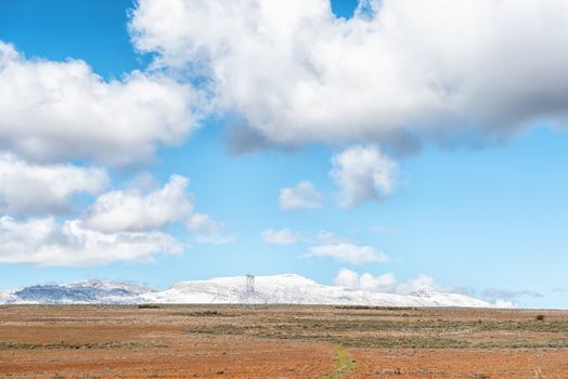 CERES, SOUTH AFRICA, AUGUST 8, 2018: Farm landscape on road R46 near Ceres in the Western Cape Province. Electricity infrastructure and snow on Matroosberg are visible