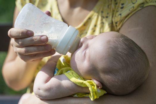 Baby sucks on a bottle. Baby in mother's hands