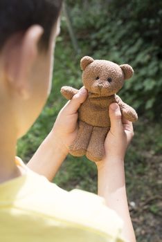 Child hold teddy in a garden. 