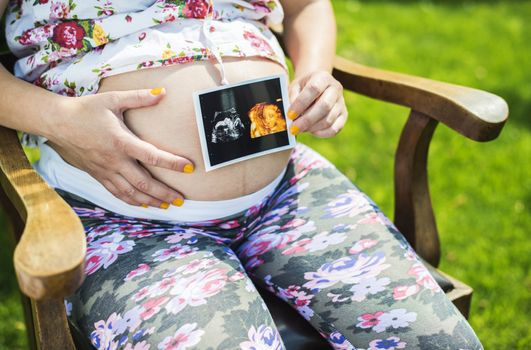 Pregnant women hold picture of womb. Daylight in the garden