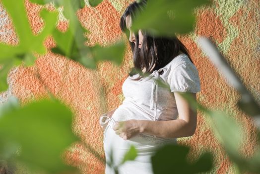 Pregnant women in front of orange wall. White dress