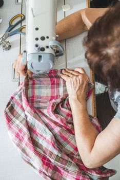 Women sew on sewing machine. White machine