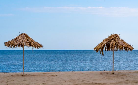 damaged two straw beach umbrellas on an empty seashore on a clear day