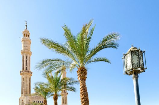 lantern street lighting two date palms two minarets of the mosque El Mustafa in Sharm El Sheikh on the background of the blue sky Egypt South Sinai.