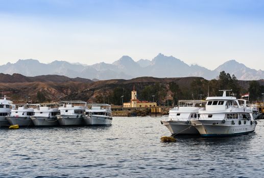 boats standing along the shore in the red sea against the background of mountains and blue sky