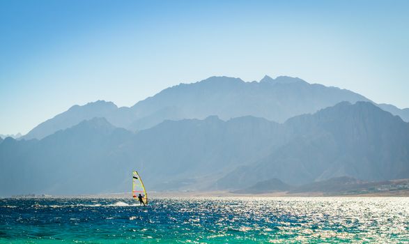 surfer rides into the sea against the backdrop of the high rocky mountains in Egypt Dahab