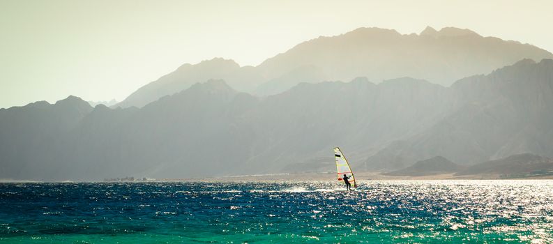 surfer rides in the Red Sea against the backdrop of a rocky coast in Egypt in the evening