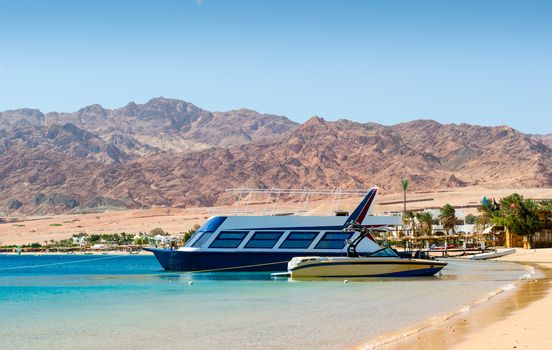 two boats at the surf on the background of the beach with palm trees and high rocky mountains in Egypt