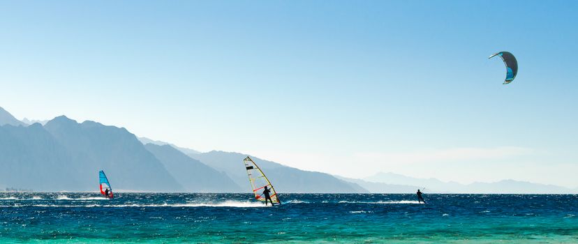 windsurfers and kitesurfers ride in the Red Sea on the background of the rocky coast in Egypt Dahab