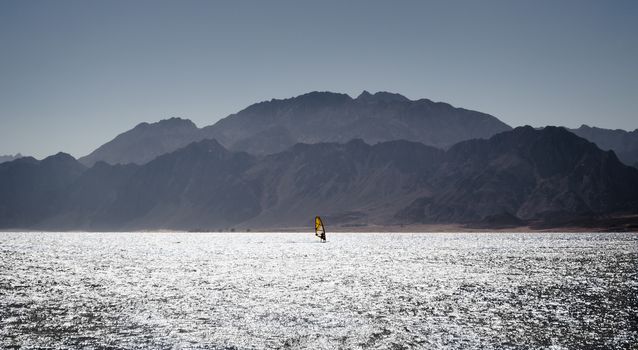 surfer rides in the Red Sea against the backdrop of the coast with high rocky mountains in Egypt Dahab