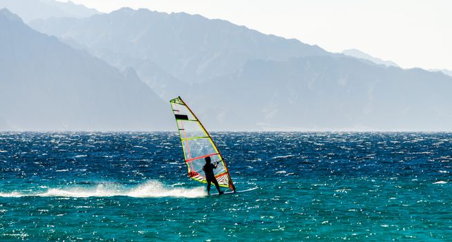 one surfer rides a sail in the Red Sea against the backdrop of the high mountains in Egypt