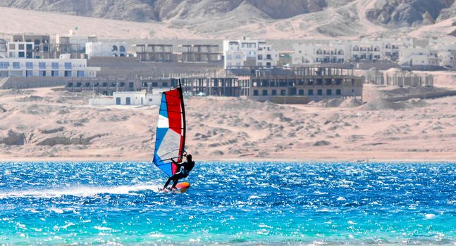 surfer with a colored sail rides in the Red Sea in Egypt against the backdrop of the beach and hotels