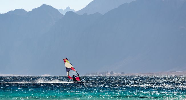 windsurfer rides in the Red Sea against the backdrop of high rocky mountains in Egypt Dahab