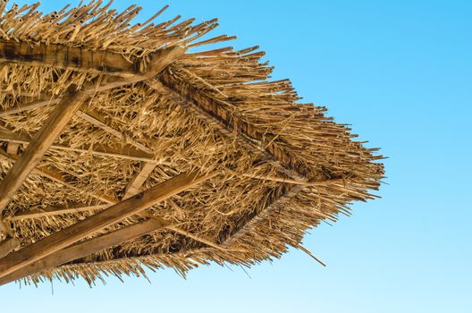 fragment of a cane beach umbrella close up against a blue sky