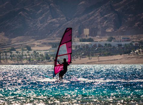 silhouette of a surfer in the Red Sea on the background of a rocky coast with palm trees and a hotel in Egypt