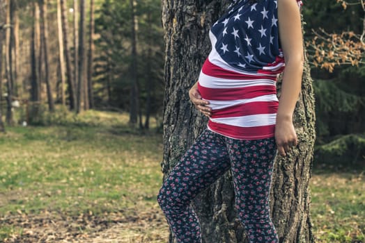 Pregnant woman in the forest. American national flag shirt