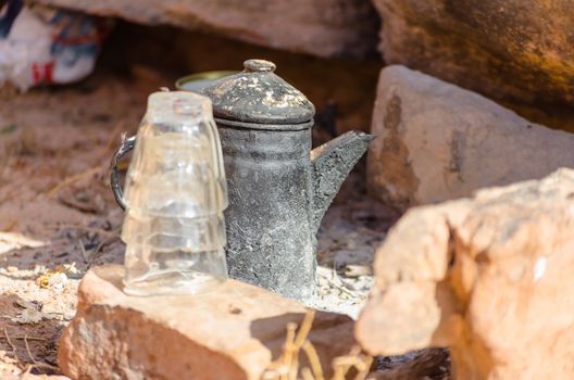 old smoked metal kettle with glasses among the stones close up