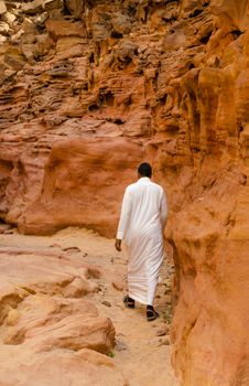 man in white arab clothing walks in a colored canyon