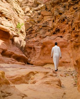 man in white arab clothing walks in a colored canyon