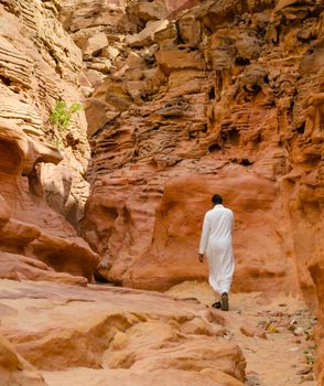 man in white arab clothing walks in a colored canyon