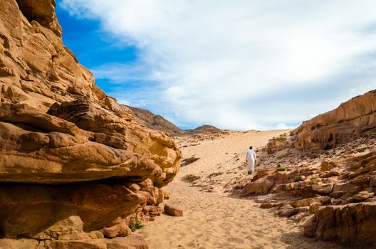 man in white arab clothing walks in a colored canyon in Egypt Dahab