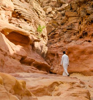 man in white arab clothing walks in a colored canyon