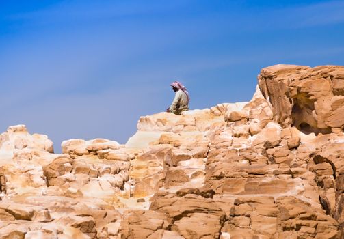 Bedouin sitting on the peak of a high stone rock against a blue sky in Egypt Dahab