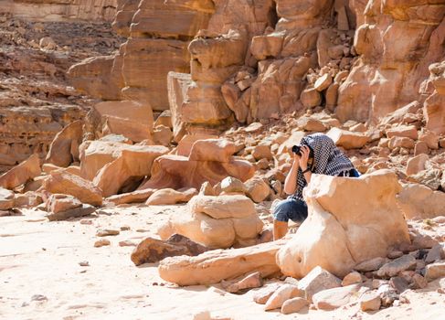 male photographer takes pictures sitting behind a stone in a canyon