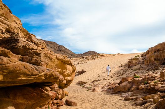 man in white arab clothing walks in a colored canyon in Egypt Dahab