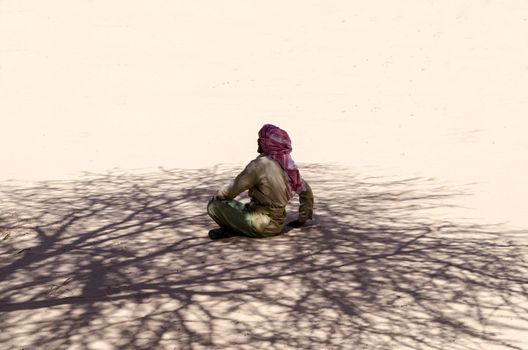 Bedouin is sitting on the sand in the shade of a tree in the desert