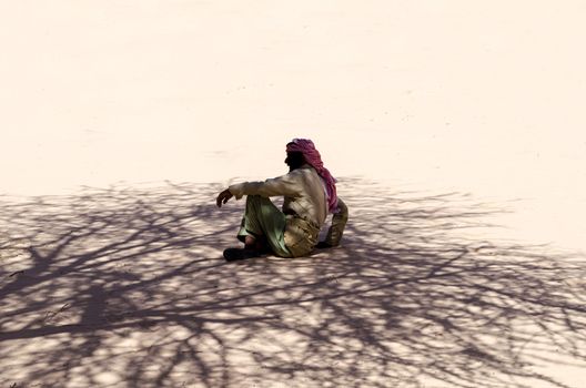 Bedouin is sitting on the sand in the shade of a tree in the desert