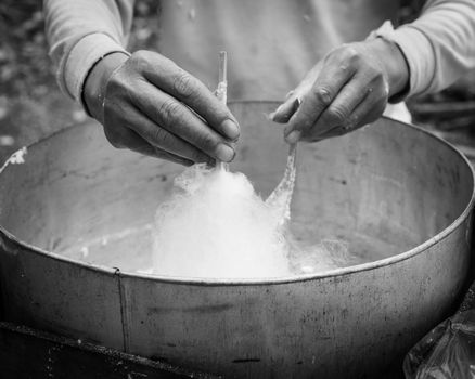 Vintage tone close-up Asian hand rolling cotton candy in floss machine in Vietnam. Process of street food making
