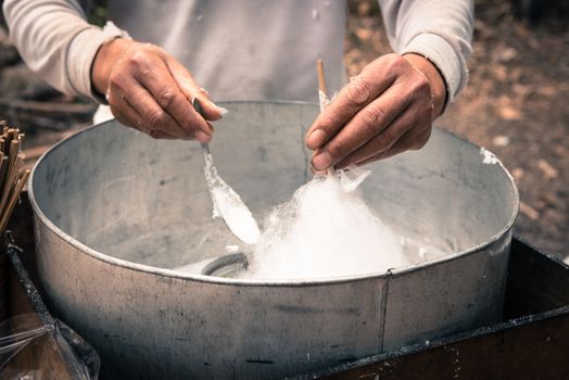 Asian hand rolling cotton candy in floss machine using bamboo stick and long spoon in Vietnam. Process of street food making