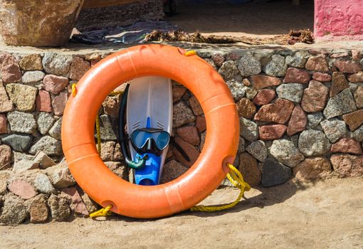 blue flippers with a swimming mask and an orange life preserver against a stone wall in Egypt