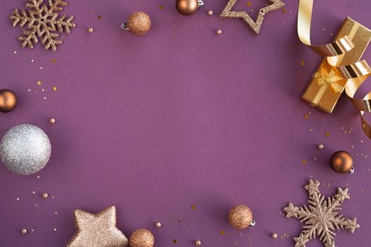 Christmas Border frame of golden glitter ornaments on purple paper background with copy space for text